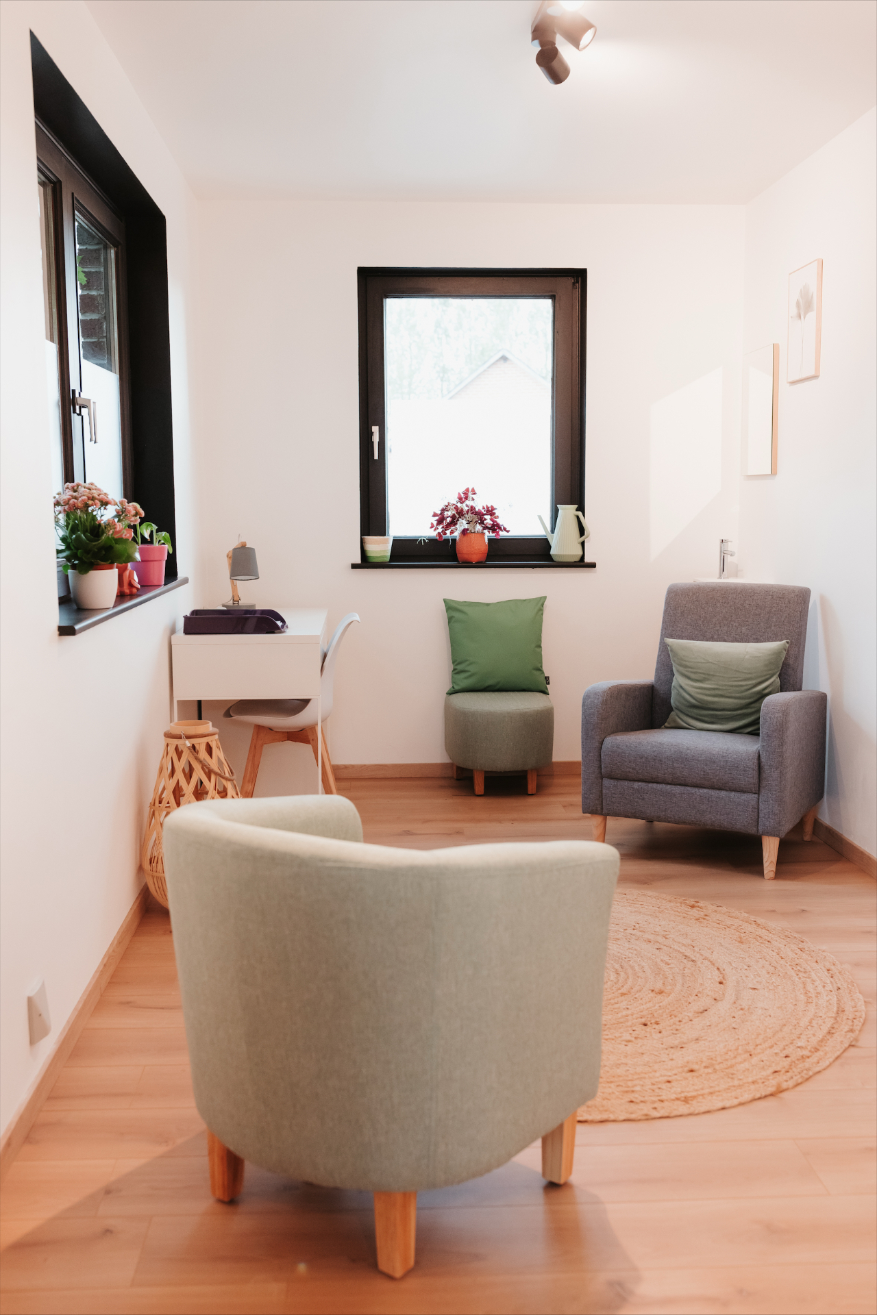 Petit salon lumineux avec fauteuils, bureau et fenêtre donnant sur la végétation